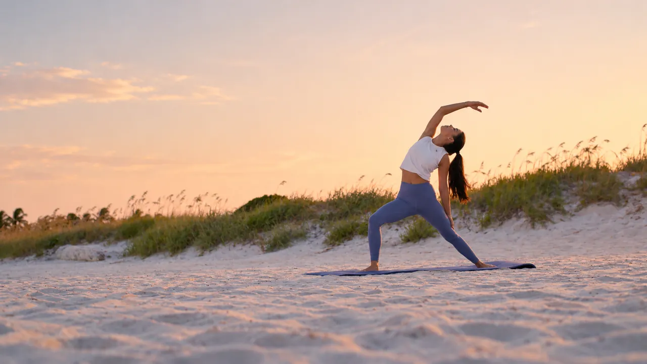 Ana practicing yoga on the beach beneath a pale sunset sky